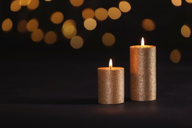 Image of Burning gold candles on black background with blurred lights, bokeh effect. Space for text