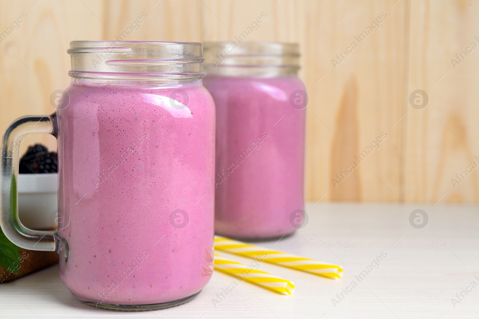 Photo of Mason jars of blackberry smoothie on white wooden table. Space for text