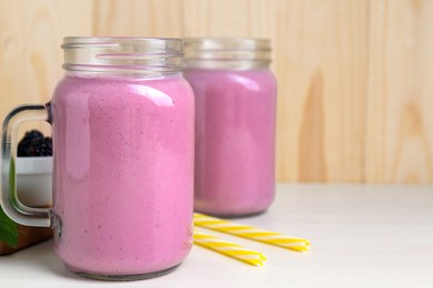 Photo of Mason jars of blackberry smoothie on white wooden table. Space for text