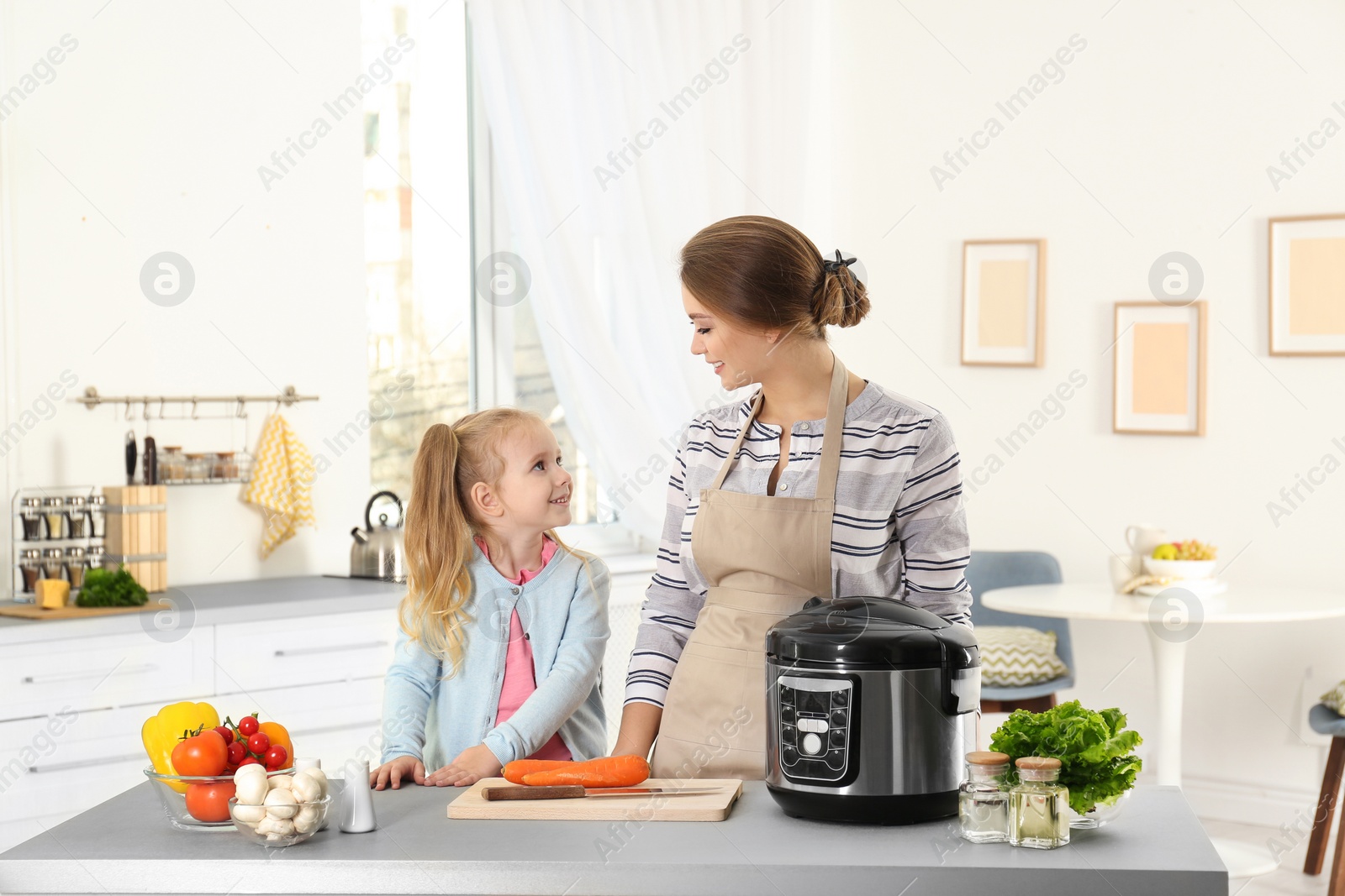 Photo of Mother and daughter preparing food with modern multi cooker in kitchen