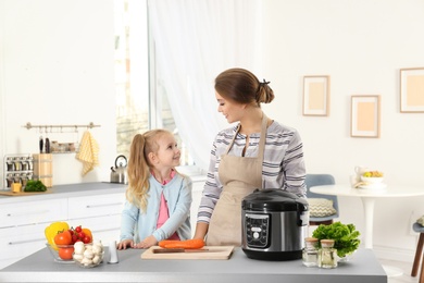 Mother and daughter preparing food with modern multi cooker in kitchen