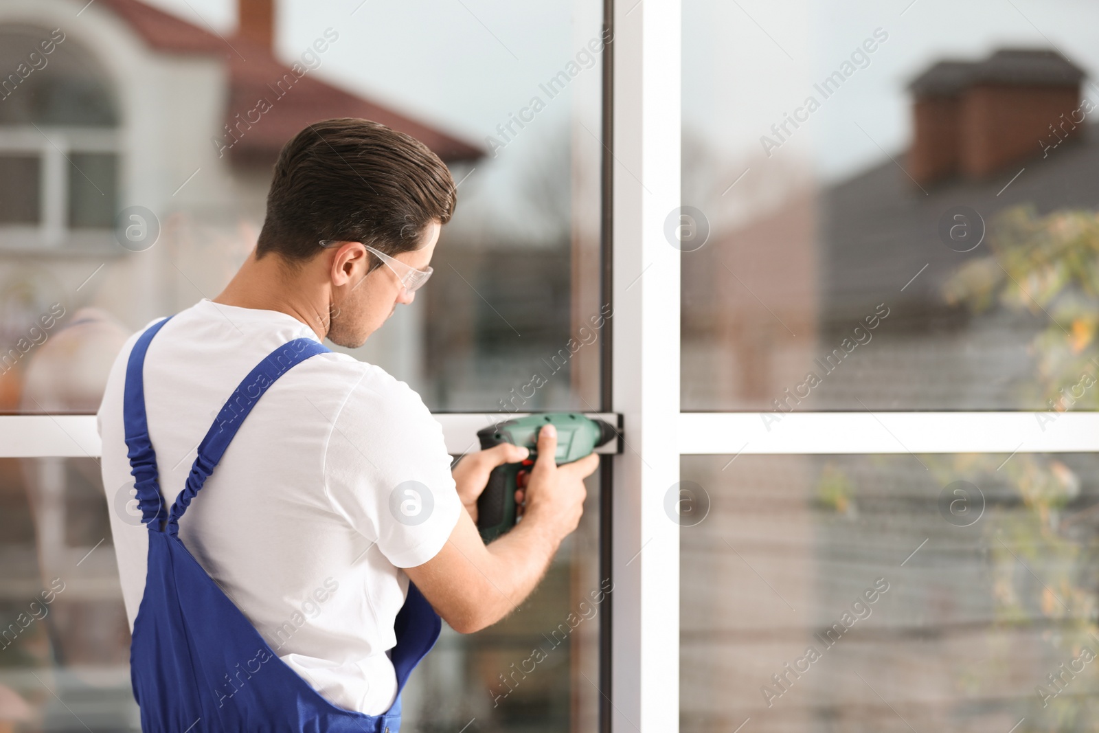 Photo of Construction worker repairing plastic window with electric screwdriver indoors