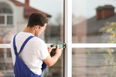 Construction worker repairing plastic window with electric screwdriver indoors