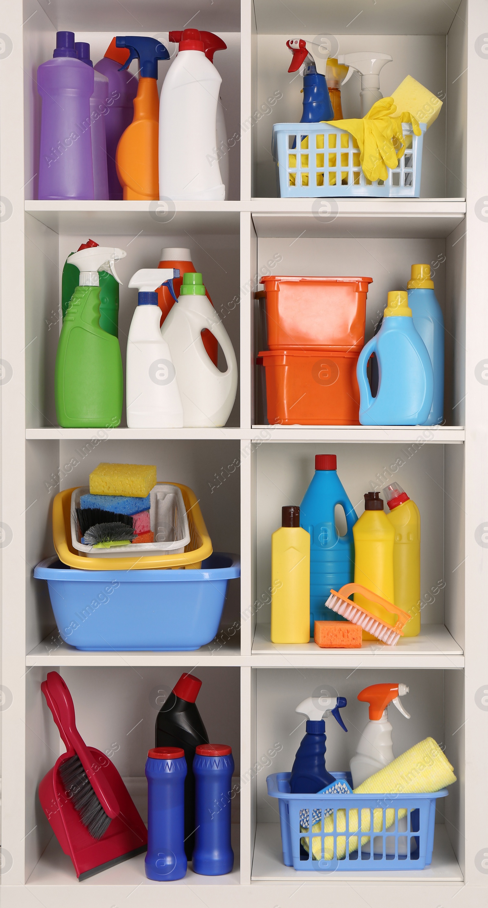 Photo of Shelving unit with detergents and cleaning tools near white wall indoors