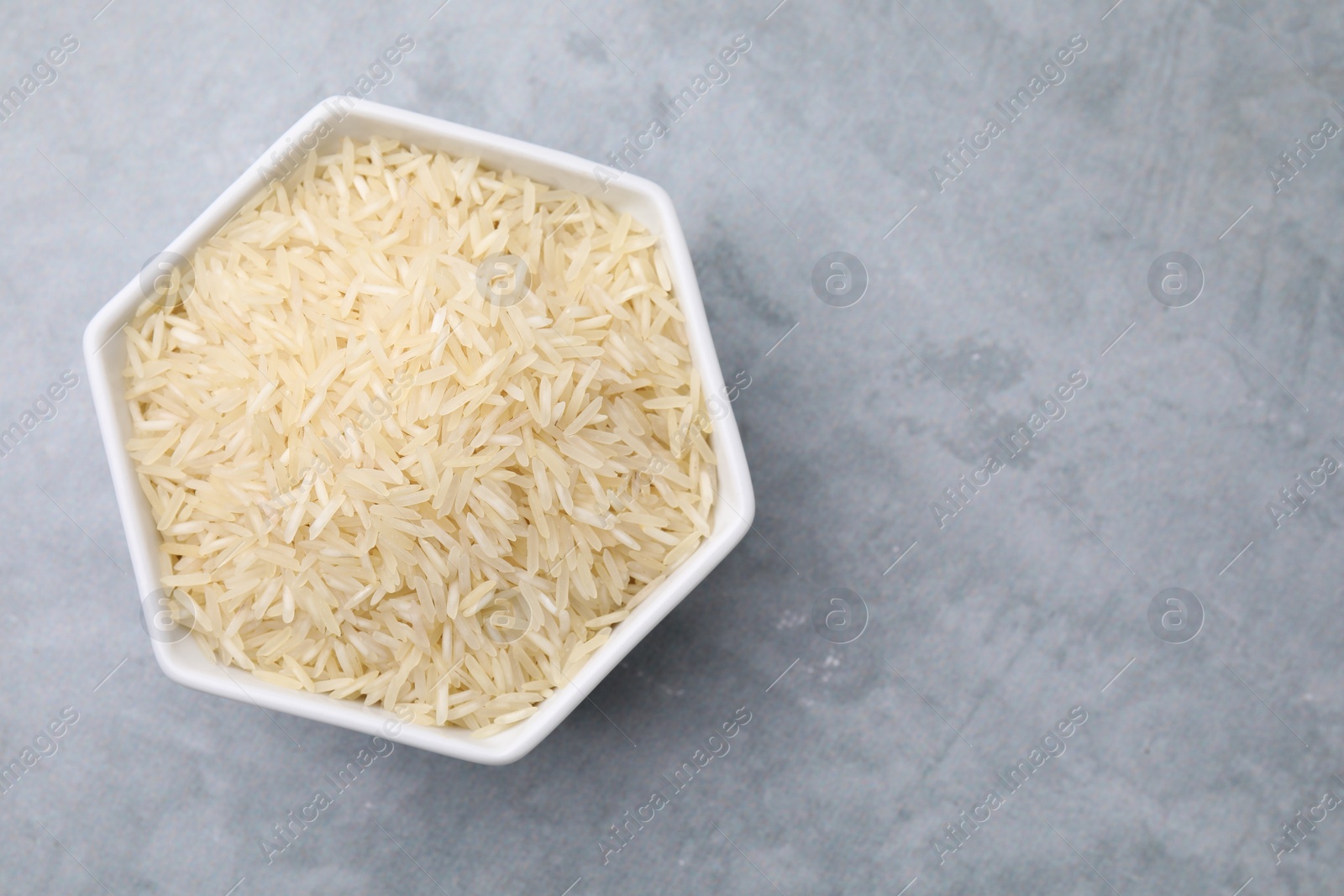 Photo of Raw rice in bowl on light grey table, top view. Space for text