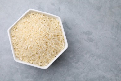 Raw rice in bowl on light grey table, top view. Space for text