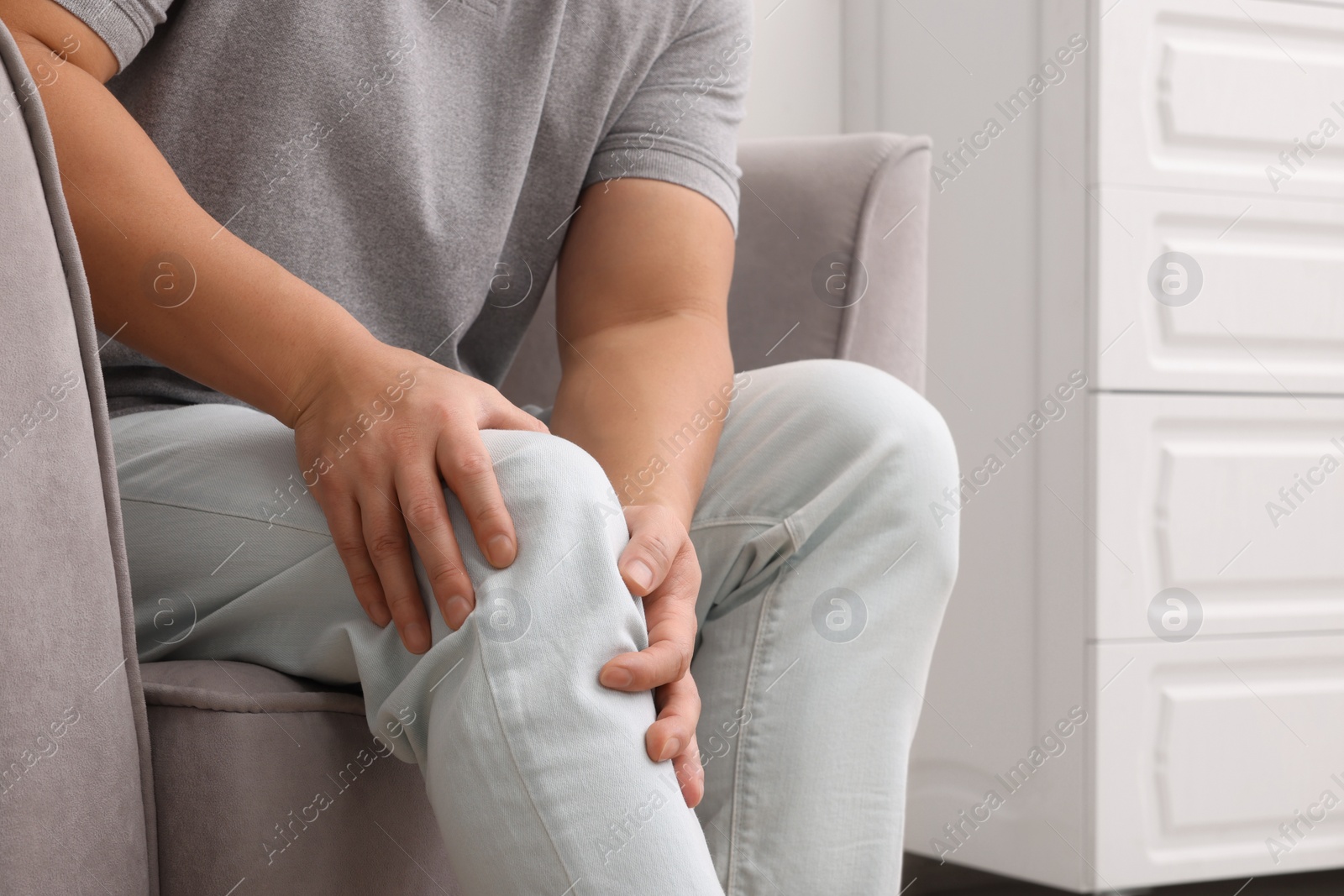 Photo of Man suffering from knee pain on armchair indoors, closeup