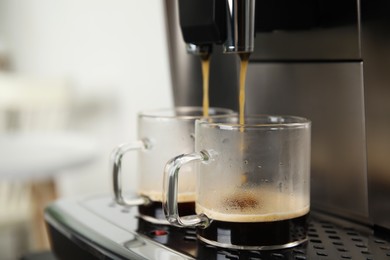 Photo of Espresso machine pouring coffee into glass cups against blurred background, closeup. Space for text