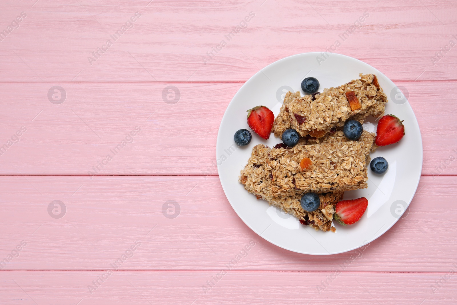 Photo of Tasty granola bars and berries on pink wooden table, top view. Space for text