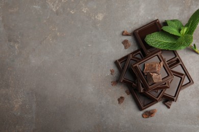 Photo of Tasty dark chocolate pieces with mint on grey table, flat lay. Space for text