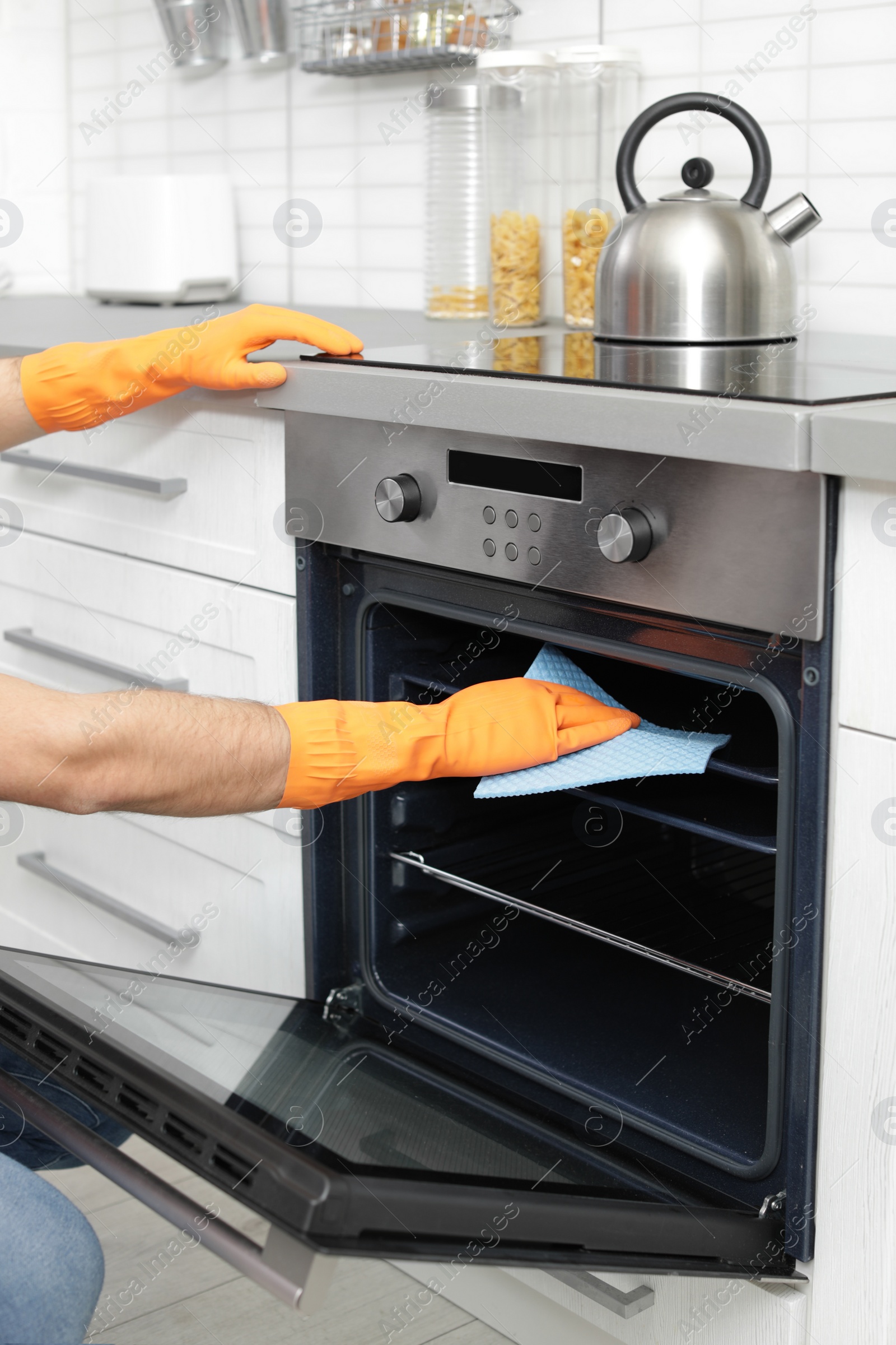 Photo of Young man cleaning oven tray with rag in kitchen