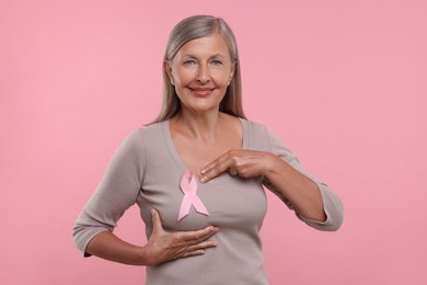 Photo of Beautiful senior woman with pink ribbon on color background. Breast cancer awareness