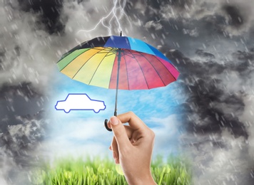 Image of Insurance concept. Woman protecting car illustration with rainbow umbrella from storm, closeup