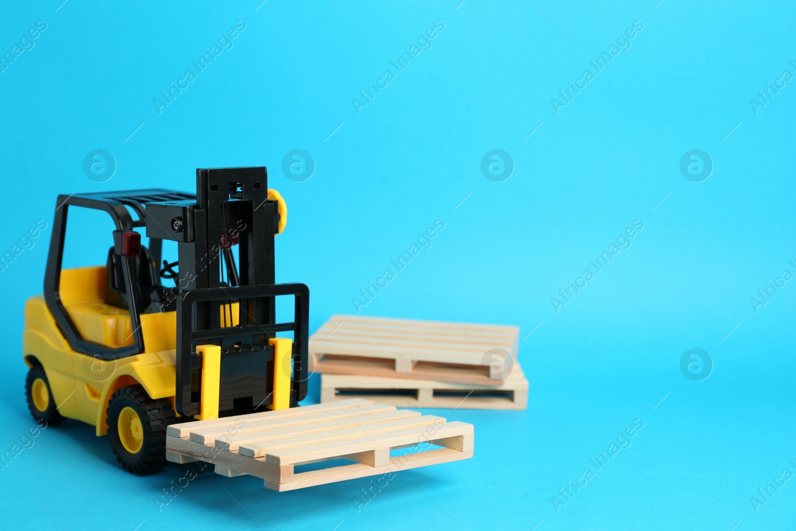 Photo of Toy forklift and wooden pallets on light blue background, space for text