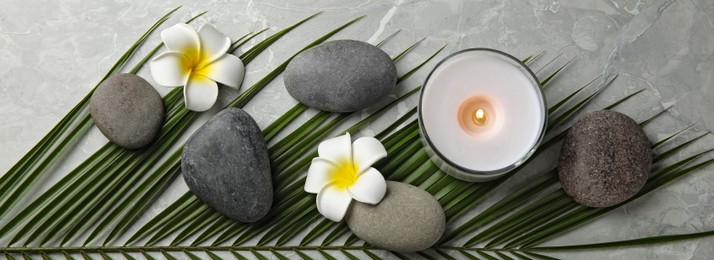 Image of Spa treatment. Flat lay composition with stones, plumeria flowers and burning candle on grey table. Banner design