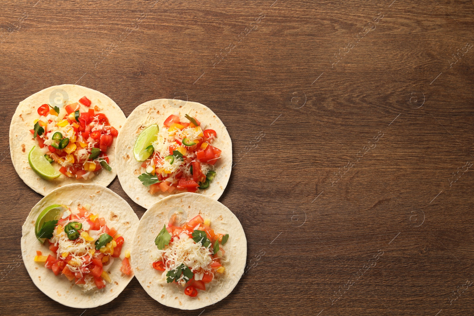 Photo of Delicious tacos with vegetables and lime on wooden table, top view. Space for text