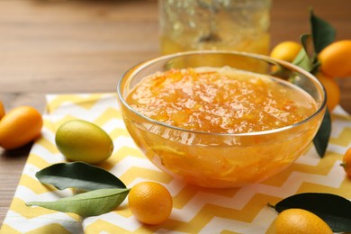 Delicious kumquat jam in bowl and fresh fruits on table, space for text