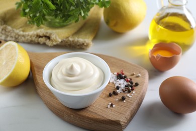 Photo of Tasty mayonnaise sauce in bowl, ingredients and spices on white table