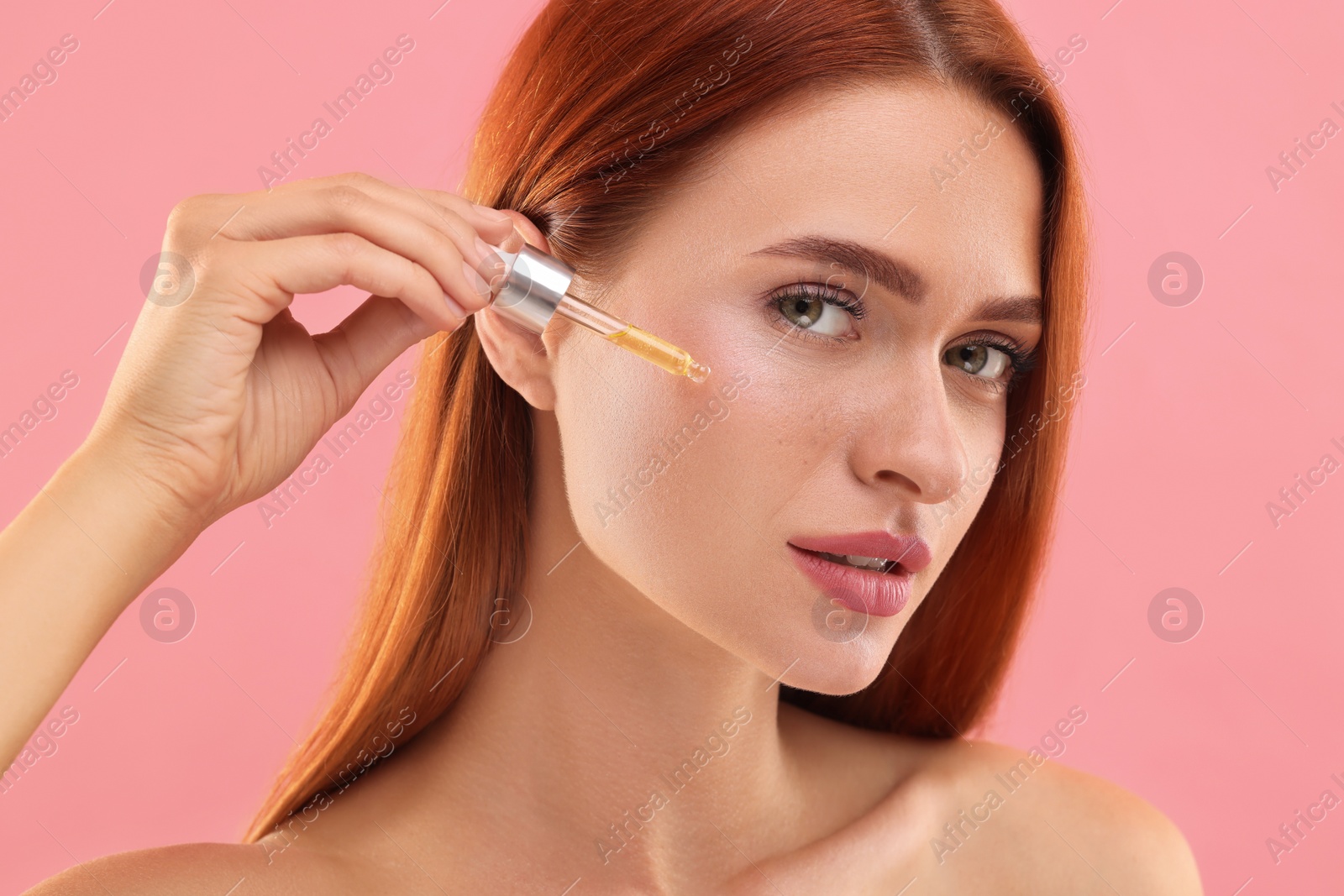 Photo of Beautiful young woman applying cosmetic serum onto her face on pink background