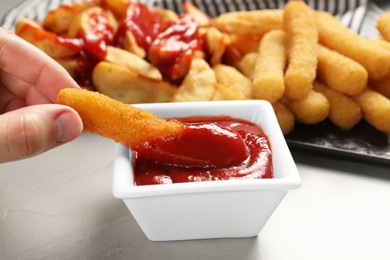 Photo of Woman dipping delicious cheese stick into bowl with ketchup on light grey table, closeup