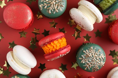 Beautifully decorated Christmas macarons and confetti on red background, flat lay