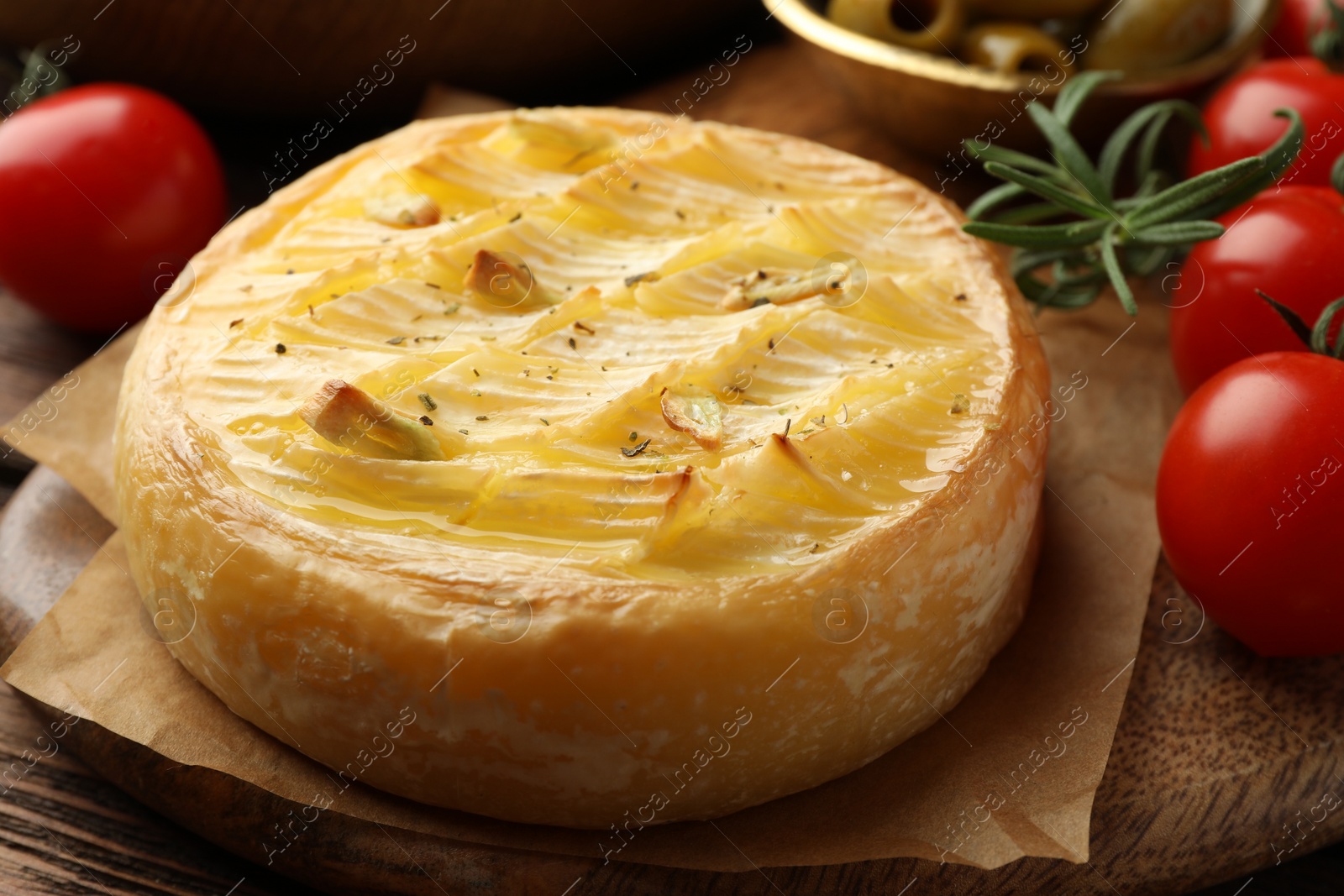 Photo of Tasty baked brie cheese with rosemary and cherry tomatoes on wooden board, closeup
