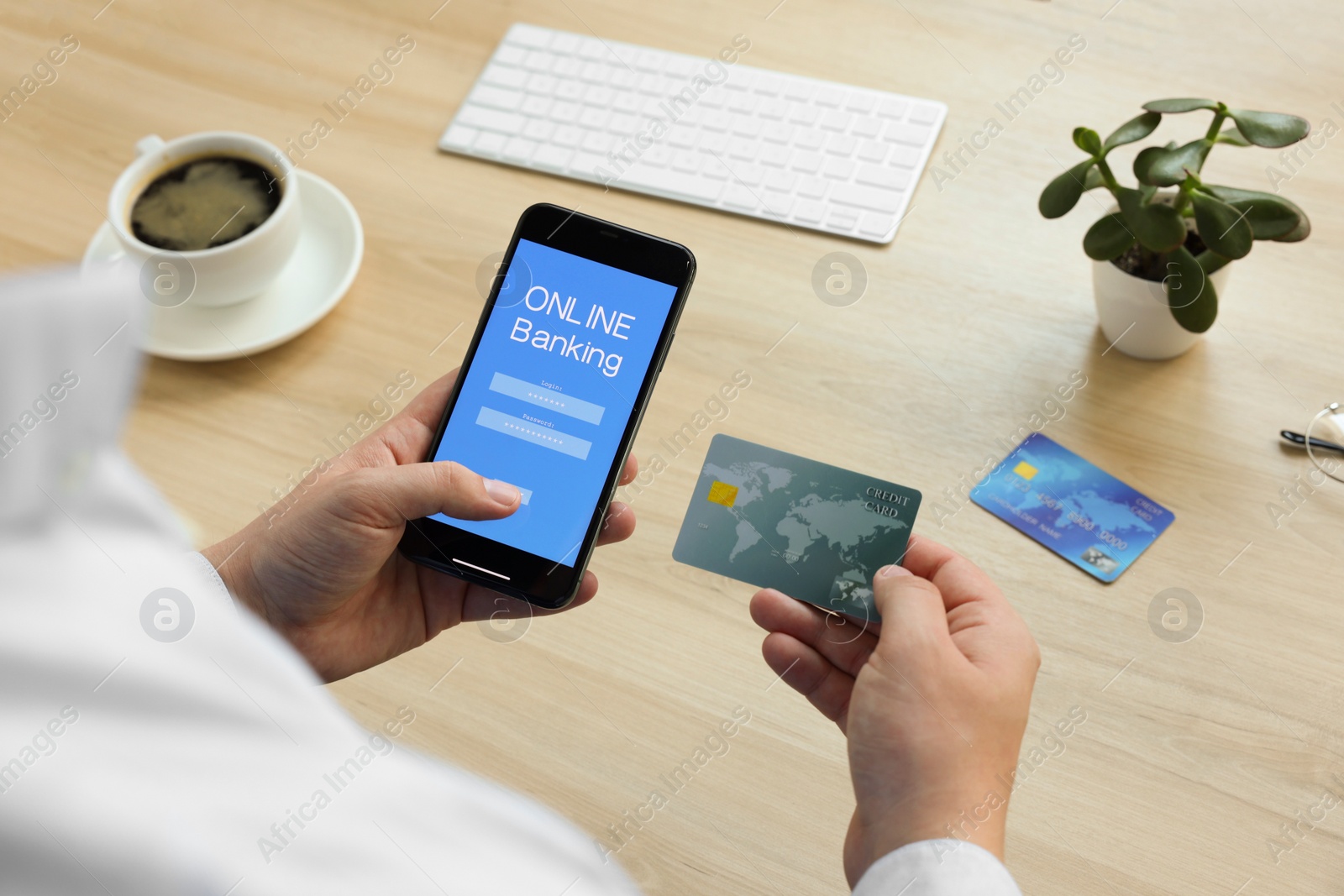 Photo of Man using online banking app on smartphone and credit card at wooden office table, closeup