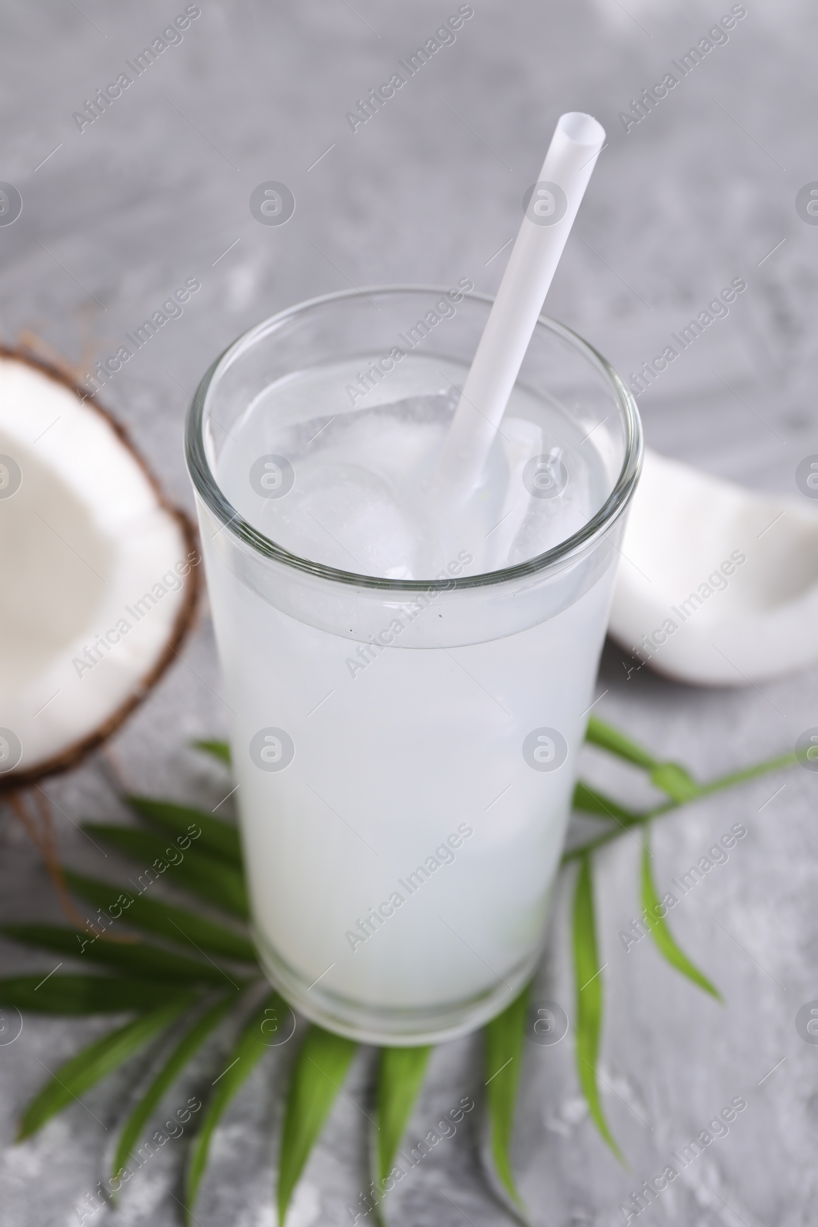 Photo of Glass of coconut water with ice cubes, palm leaf and nut on grey table