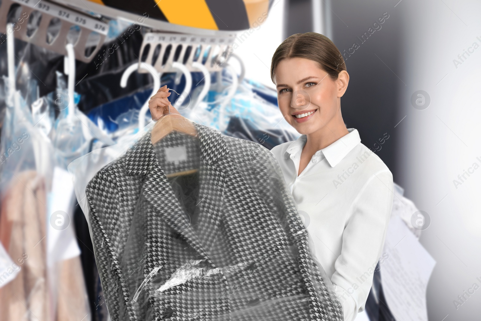 Image of Young woman holding hanger with jacket in plastic bag indoors. Dry-cleaning service
