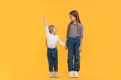 Photo of Full length portrait of cute little sisters on orange background