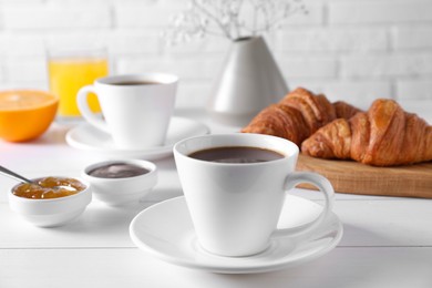 Cup of coffee, jam and croissants on white wooden table. Tasty breakfast