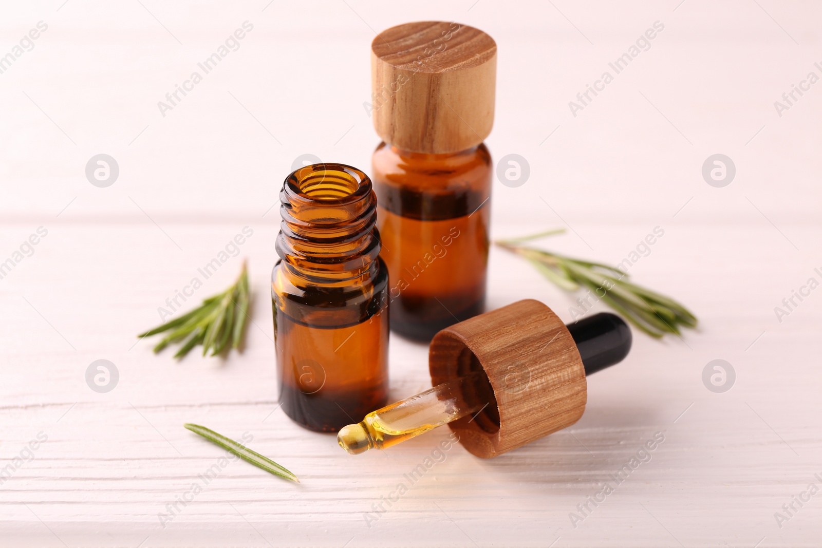 Photo of Essential oil in bottles, dropper and rosemary on white wooden table