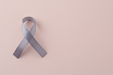 Photo of Grey awareness ribbon on beige background, top view. Space for text