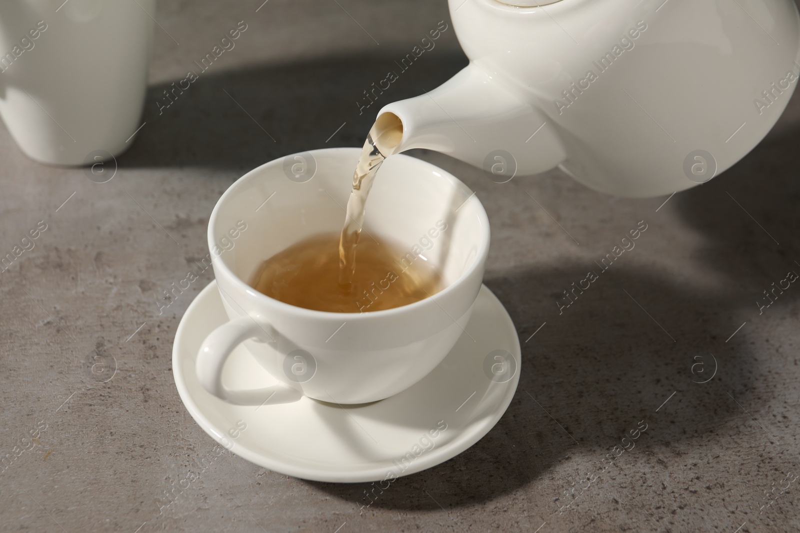 Photo of Pouring aromatic tea in cup at gray table, closeup