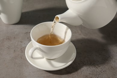 Photo of Pouring aromatic tea in cup at gray table, closeup