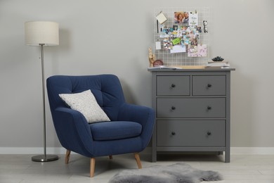 Photo of Stylish room interior with vision board, armchair and chest of drawers