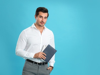 Young male teacher with notebooks on light blue background. Space for text