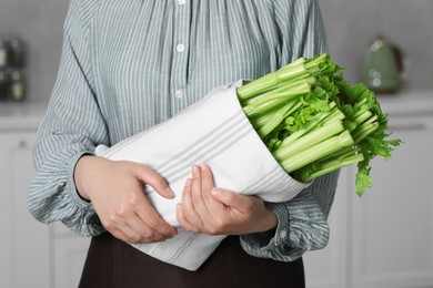 Woman with fresh green celery in kitchen, closeup