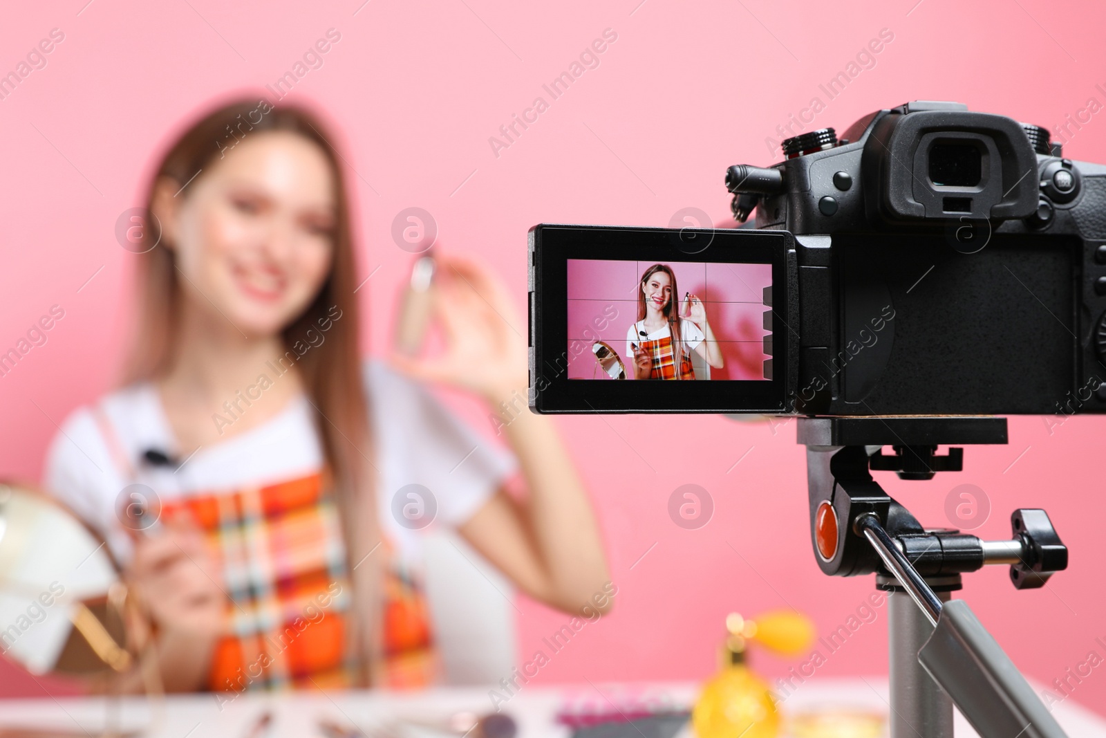 Photo of Beauty blogger filming make up tutorial on pink background, focus on camera