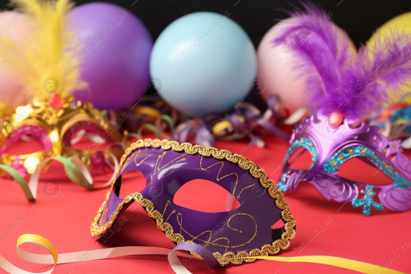 Photo of Beautiful carnival mask and party decor on red table, closeup