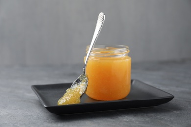 Delicious orange marmalade in jar and spoon on grey table