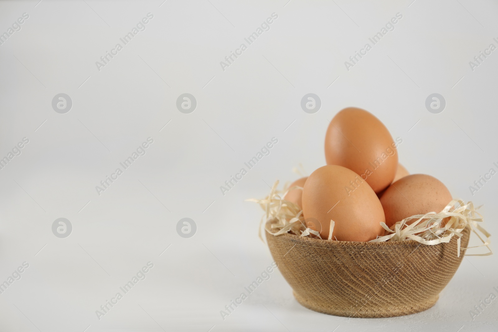 Photo of Raw chicken eggs and decorative straw on white table. Space for text