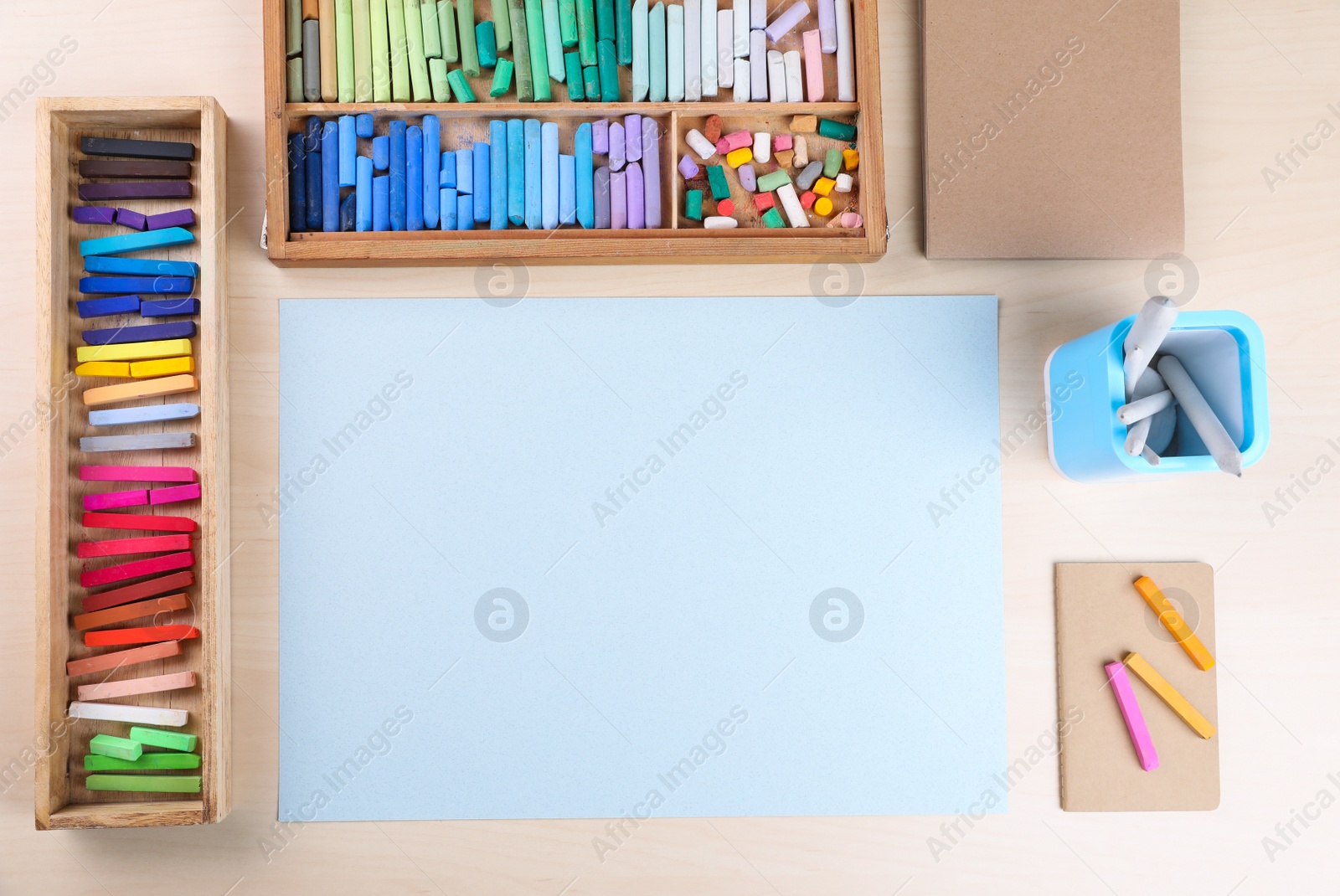 Photo of Layout with blank paper, soft pastels and other drawing supplies on wooden table at artist's workplace, top view. Space for design