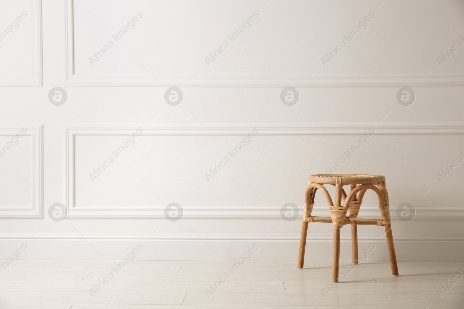 Photo of Stylish wooden stool near white wall, space for text. Interior element