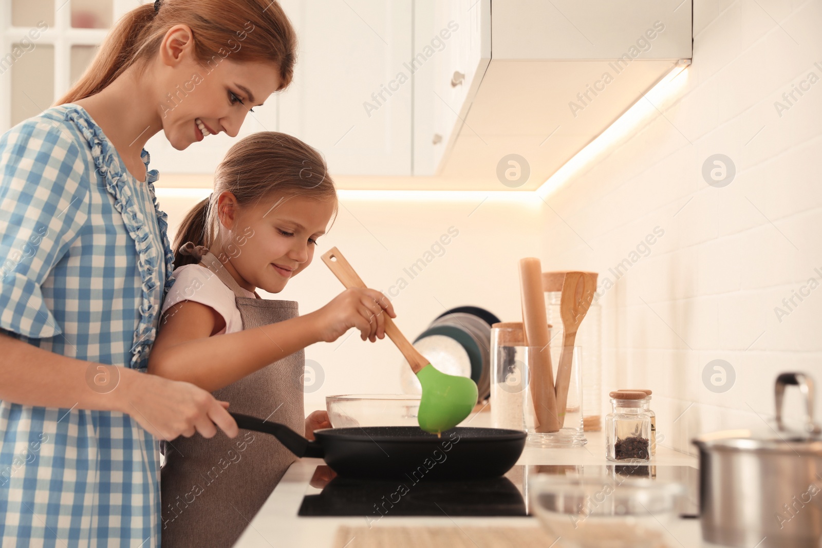 Photo of Mother and daughter making pancakes together in kitchen