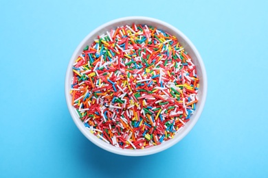 Photo of Colorful sprinkles in bowl on light blue background, top view. Confectionery decor