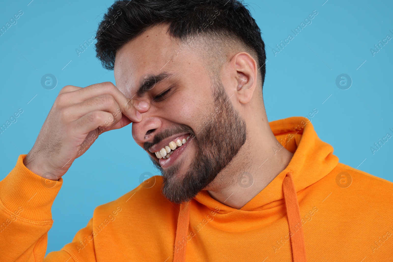 Photo of Handsome young man laughing on light blue background, closeup