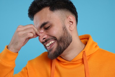 Handsome young man laughing on light blue background, closeup