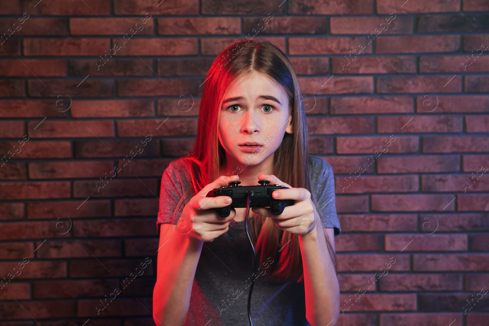 Photo of Teenage girl playing video games with controller near brick wall