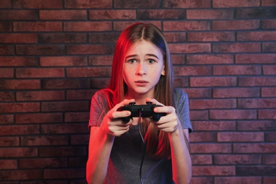 Photo of Teenage girl playing video games with controller near brick wall